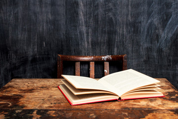 Open book on desk by blackboard