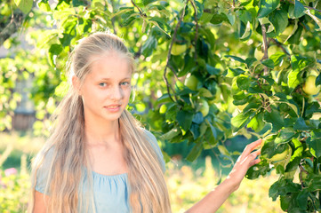 Outdoor portrait of beautiful blonde girl posing near apple tree