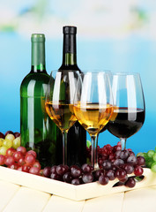 Obraz premium Wine bottles and glasses of wine on tray, on bright background