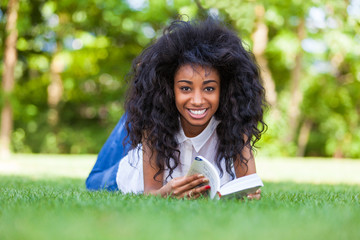 Fototapeta premium Young student girl reading a book in the school park - African p
