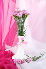 Many small pink cloves in vase on light fabric background