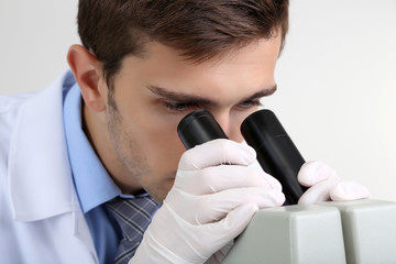 Naklejka premium Young laboratory scientist looking at microscope in lab