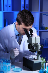 Young laboratory scientist looking at microscope in lab