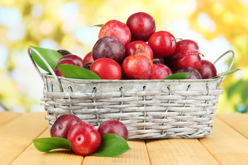 Ripe plums in basket on wooden table on natural background