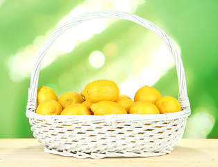Ripe lemons in wicker basket on table on bright background