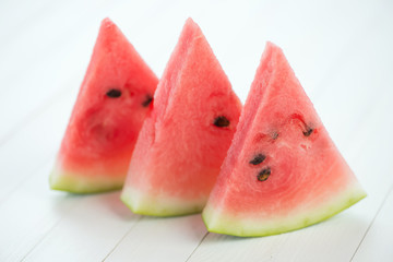 Three slices of ripe watermelon over white wooden boards