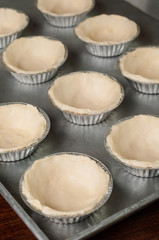 Obraz na płótnie Canvas Raw dough in tartlet tins on baking tray.