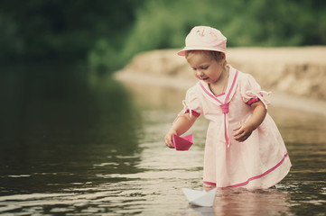 little girl plays with paper boats in river