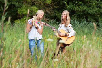 Two retro blonde 70s hippie girls making music with acoustic gui