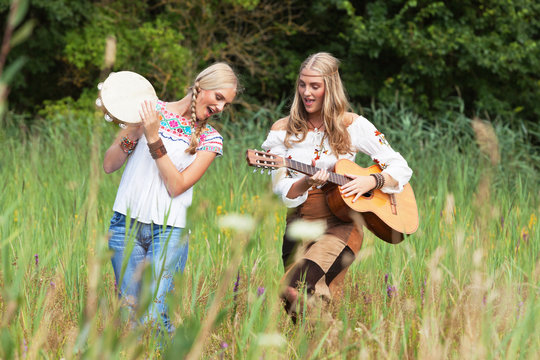 Two retro blonde 70s hippie girls making music with acoustic gui