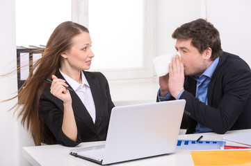 Flu. Man sneezing while sitting near his coworker