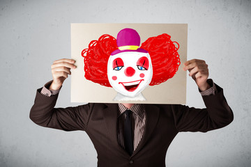 Businessman holding a cardboard with a clown on it in front of h