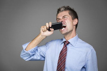 very angry businessman si biting his mobile phone