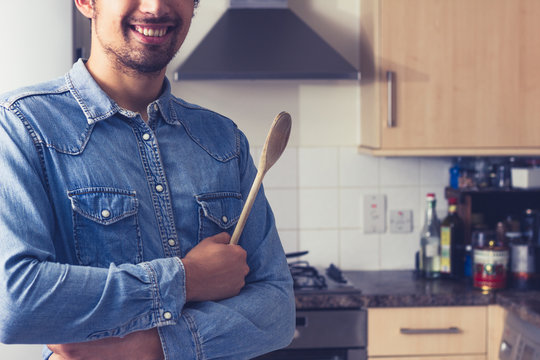 Happy young man with wooden spoon in kitchen
