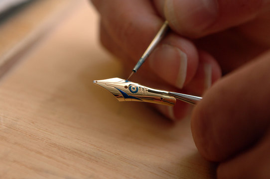 Closeup: Hand mit Pinsel bemalt goldene F&uuml;llerfeder