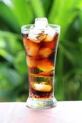 Refreshing Brown cola Soda with Ice cube on a green tree background
