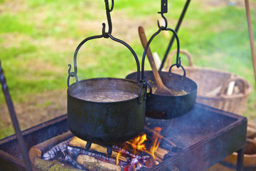 Cooking meal outdoors with pots on an open fire .