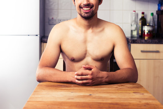 Naked man sitting in his kitchen