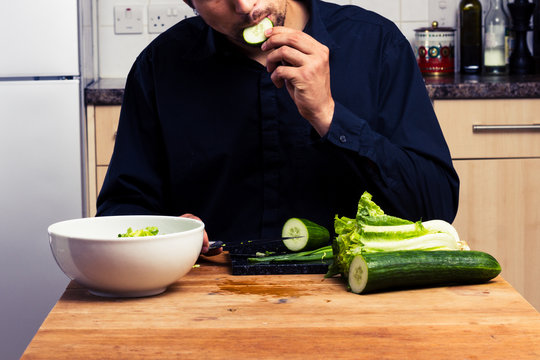 Man making a salad and eating cucumber