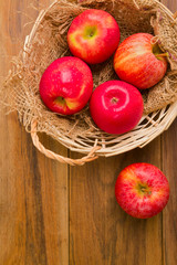 Fresh red apples in basket over wooden background