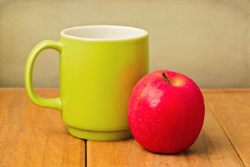 Red apple and green cup on wooden table over grunge background