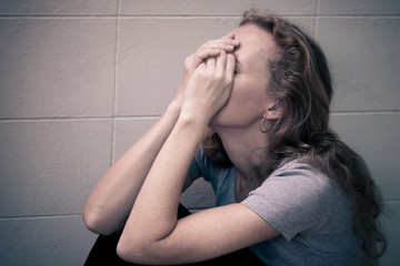 one sad woman sitting on the floor near a wall and holding her h