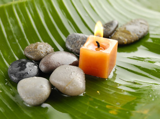 Candle and stones on wet banana leaf