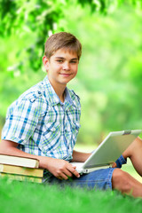 Teen boy with books and laptop in the park.