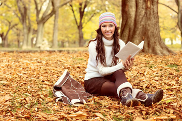 woman sitting on the autumn leaves and reading book