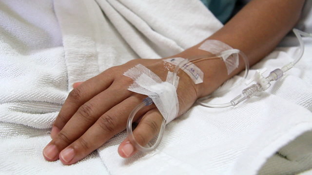 closeup saline drip into patient hand on bed in hospital