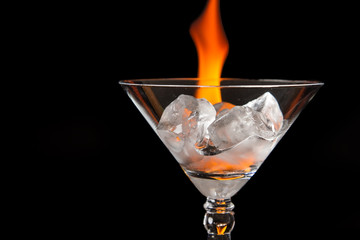 Ice cubes in glass with flame on shiny black surface
