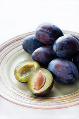 Fresh plums on plate  over light background