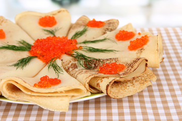 Delicious pancakes with red caviar on table in room