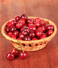 Cherry berries in wicker basket on wooden table close-up