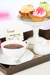 Cup of tea with cakes on wooden tray on table in room