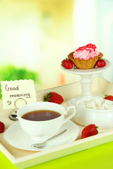 Cup of tea with cakes on wooden tray on table in room
