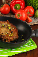 Piece of fried meat on pan on wooden table close-up