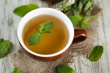 Cup of herbal tea with fresh mint flowers on wooden table