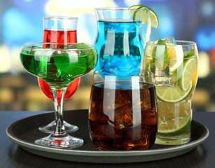 Many glasses of cocktails on tray on table, on bright