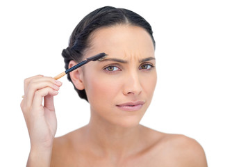 Fototapeta premium Frowning young brunette using eyebrow brush