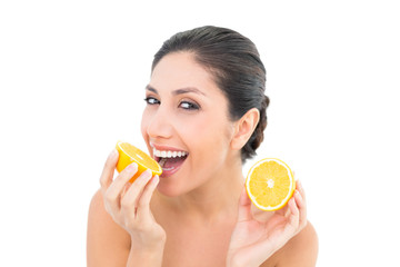 Pretty brunette holding two orange halves and smiling at camera