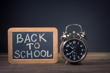 Back to School on a blackboard, alarm clock in front of black