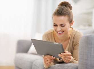 Happy young woman with tablet pc laying on sofa