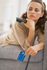 Closeup on credit card in hand of concerned woman with phone