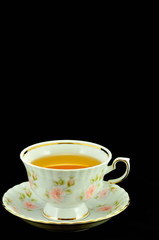 porcelain tea cup full of tea and green teapot on a black backgr