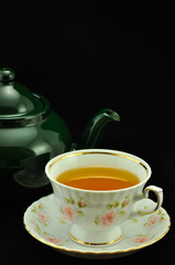 porcelain tea cup full of tea and green teapot on a black backgr
