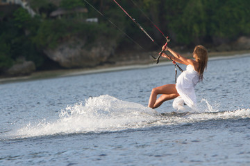 young beautiful woman in wedding dress kitesurfing on water back