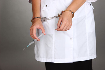 Doctor with syringe in handcuffs on grey background