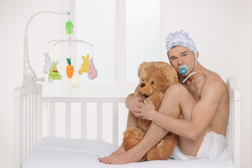 Big baby. Infant adult man in diaper holding teddy bear while si - obrazy, fototapety, plakaty