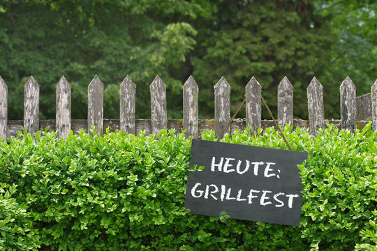 Alter Gartenzaun mit Tafel vor Buchsbaumhecke